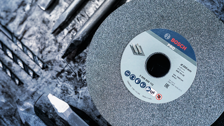 PRO Metal Grinding Wheel, 200 x 25 x 32 mm, G46 Large grinding wheel placed among several metal drill bits on a rough work surface.