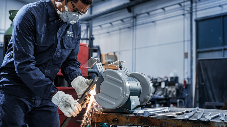 PRO Metal Grinding Wheel, 200 x 25 x 32 mm, G46 Person wearing safety equipment grinds metal on a bench grinder in a workshop.