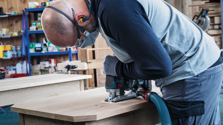 PRO Hardwood clean reverse T101BRF Jigsaw Blade, 100 mm, 5 pcs A person wearing safety equipment uses a jigsaw to cut wood on a workbench.