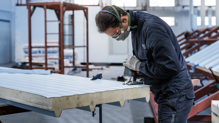 PRO Metal Sandwich T718BF Jigsaw Blade, 180 mm, 3 pcs A person wearing safety equipment cuts sheet metal with a power tool.