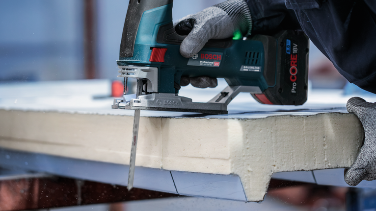 PRO Metal Sandwich T718BF Jigsaw Blade, 180 mm, 3 pcs A person wearing safety equipment cuts foam board with a cordless jigsaw.