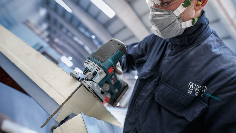 PRO Metal Sandwich T718BF Jigsaw Blade, 180 mm, 3 pcs Person wearing safety equipment cuts foam insulation with a power jigsaw.