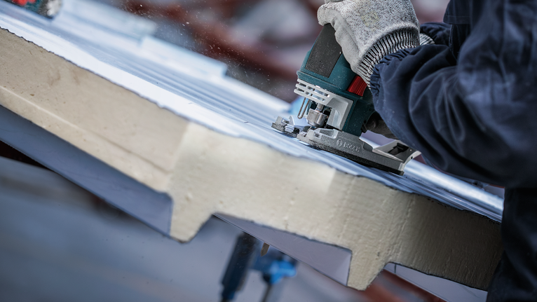 PRO Metal Sandwich T718BF Jigsaw Blade, 180 mm, 3 pcs A person wearing safety equipment cuts insulation material with a jigsaw.