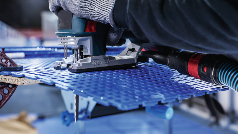 PRO Soft Material T313AW Jigsaw Blade, 152 mm, 3 pcs Person wearing safety equipment guides a jigsaw to cut a blue perforated sheet.