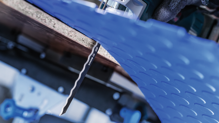 PRO Soft Material T313AW Jigsaw Blade, 152 mm, 3 pcs A person wearing safety equipment uses a jigsaw to cut a blue plastic sheet.