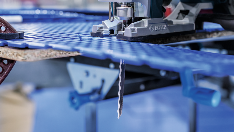 PRO Soft Material T313AW Jigsaw Blade, 152 mm, 3 pcs Jigsaw cutting through a sheet of blue plastic in a workshop.