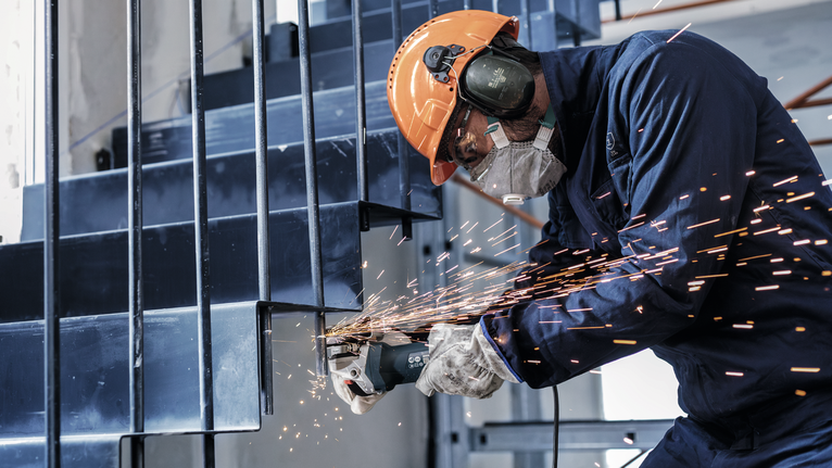 Person wearing safety equipment grinds a metal staircase, sending sparks outward.