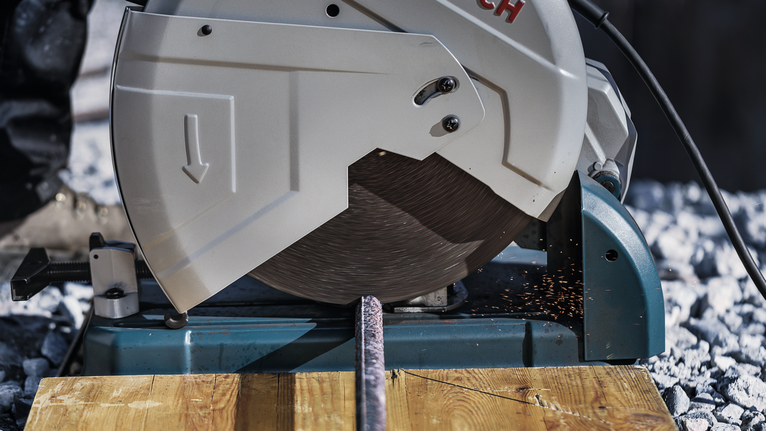 Metal cutting saw slicing through a rebar, producing sparks on a wooden surface.