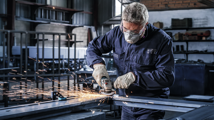 A worker wearing safety equipment grinds metal, creating sparks in a factory.