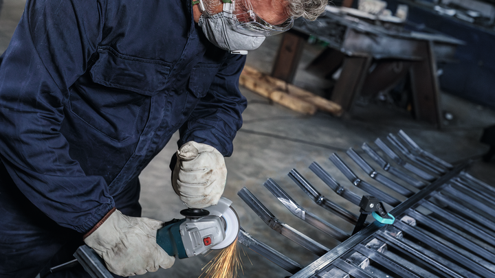 Person wearing safety equipment grinds metal, sparks flying from the tool.