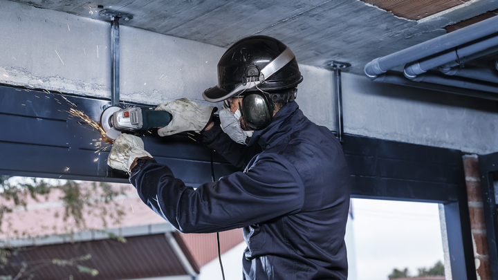 Person wearing safety equipment grinds a metal beam on a building site.
