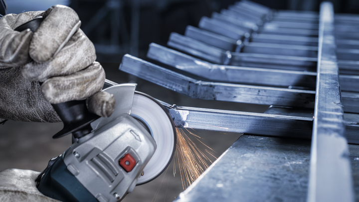 Worker wearing safety equipment grinds a metal frame with an angle grinder.