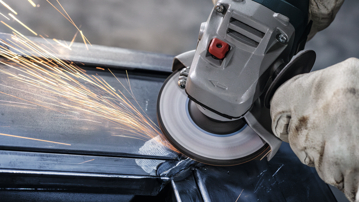Gloved worker grinds the edge of metal, sparks flying from the abrasive wheel.