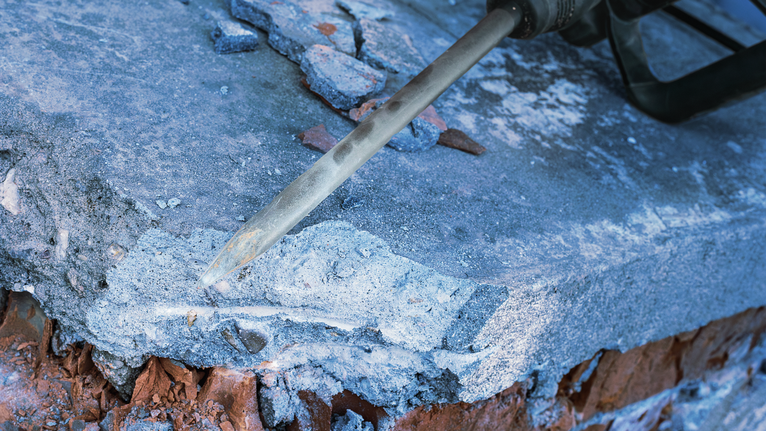 A demolition hammer breaks concrete along the edge of a brick structure.