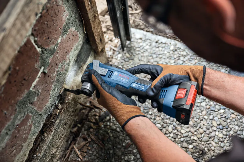 A person wearing safety equipment uses a cordless multi-cutter to cut into mortar near bricks.