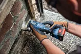 Person wearing safety equipment uses cordless multi-cutter on brick wall.