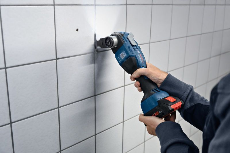 A person cuts into wall tiles using a cordless multi-cutter.