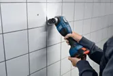 A person cuts into wall tiles using a cordless multi-cutter.