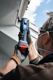 A person wearing safety equipment uses a cordless multi-cutter to trim a window frame.