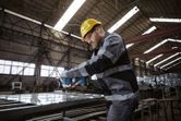 A person wearing safety equipment uses a power tool to fasten bolts on a metal frame.