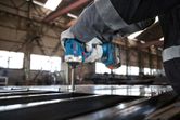 A person wearing safety equipment uses a cordless power tool to fasten screws into metal.