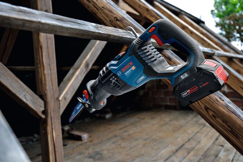 Cordless reciprocating saw resting on a wooden beam at a construction site.
