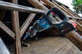 Cordless reciprocating saw resting on a wooden beam at a construction site.