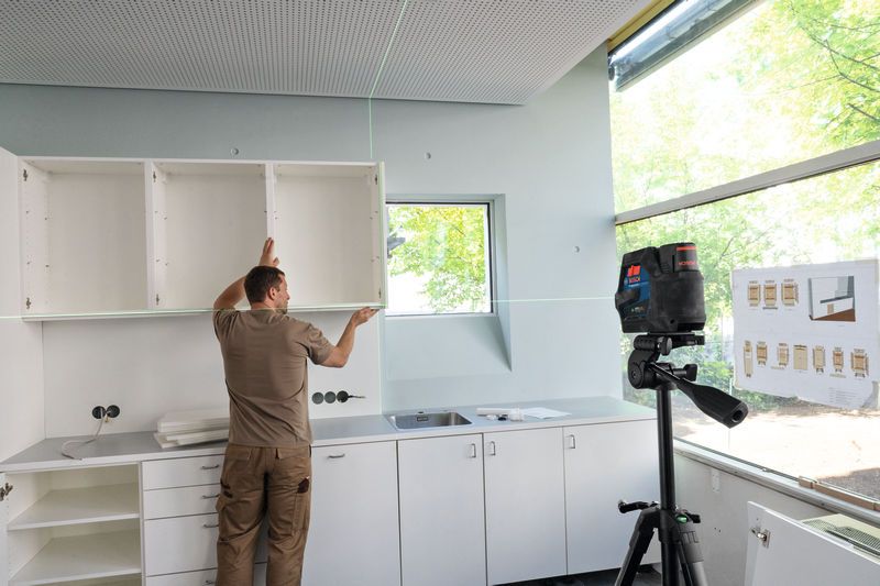 Person aligns wall cabinets using a laser leveling tool in a kitchen installation.