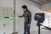 Person marks a wall using a laser leveling tool projecting a green horizontal line.