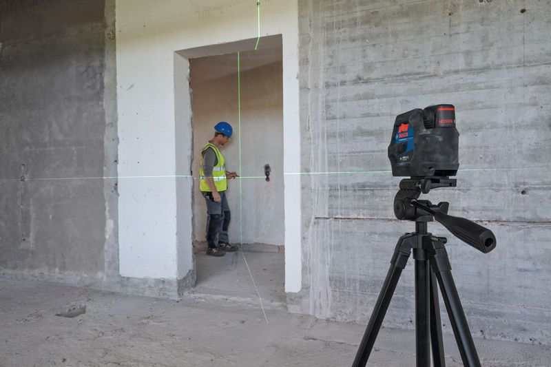 Laser leveling tool projects green lines in a room as a person wearing safety equipment works.