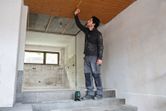 A person wearing safety equipment measures a ceiling using a laser leveling tool.