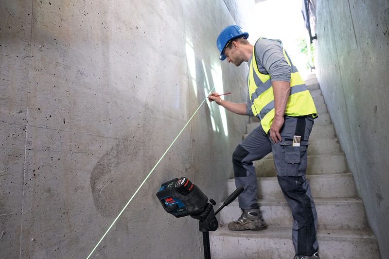 A person wearing safety equipment marks a wall using a laser leveling tool.