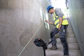 A person wearing safety equipment marks a wall using a laser leveling tool.