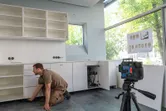 Person aligns cabinets in a room using a laser leveling tool on a tripod.