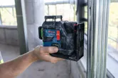Person holding a laser leveling tool aligned to a metal frame indoors.