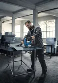 A person wearing safety equipment uses a cordless jigsaw to cut sheet metal in a workshop.