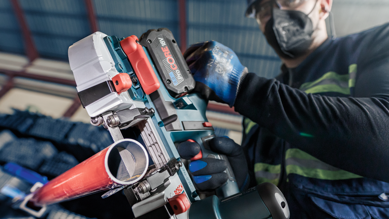 PRO CB4424 Band Saw Blade, 1140 mm, 2 pcs Person wearing safety equipment cuts a red pipe using a power tool.