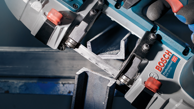 PRO CB4418 Band Saw Blade, 1140 mm, 2 pcs Person wearing safety equipment cuts a metal beam with a portable band saw.