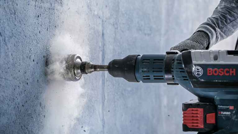 PRO SDS max-5 Core Cutter, 125 x 80 x 97 mm Person wearing safety equipment drills a hole in concrete with a rotary hammer.