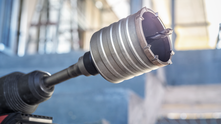 PRO SDS max-5 Core Cutter, 125 x 80 x 97 mm Close-up of a rotary hammer drill with a core bit attached in a construction area.