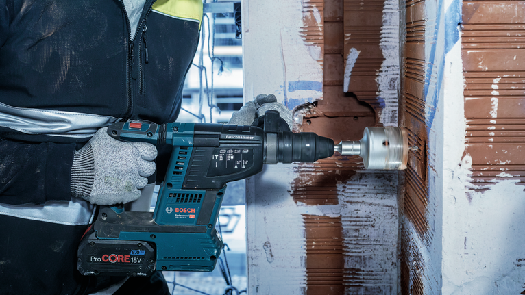 PRO SDS plus-5 Core Cutter, 68 x 50 x 80 mm A person wearing safety equipment drills a large hole in a brick wall with a power tool.