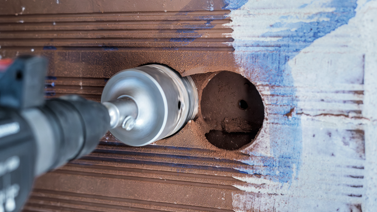 PRO SDS plus-5 Core Cutter, 68 x 50 x 80 mm Rotary drill with a hole saw attachment creates a circular opening in a tiled wall.
