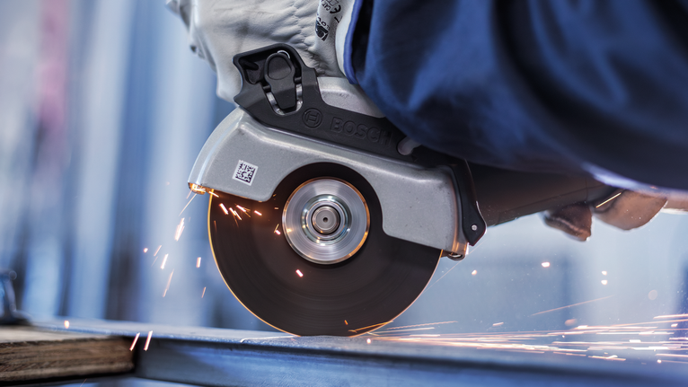 Person wearing safety equipment uses a circular saw to cut metal, creating sparks.