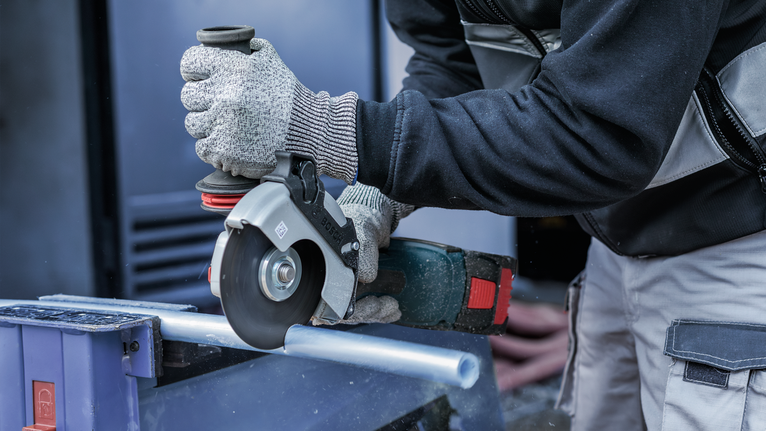 PRO Multi Material Cutting Disc, 105 x 1 x 16 mm Person wearing safety equipment cuts a metal pipe with a power tool.