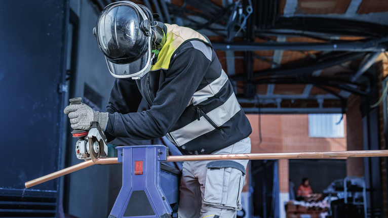 PRO Multi Material Cutting Disc, 105 x 1 x 16 mm A person wearing safety equipment grinds a copper pipe supported on a stand.