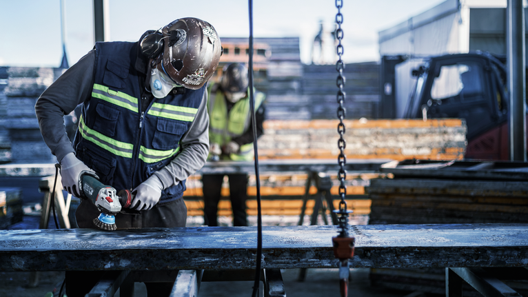 PRO Metal heavy Cup Brush, 75 x 0.5 mm, Thread A person wearing safety equipment grinds a metal surface at a construction site.