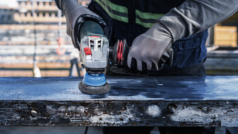 PRO Metal heavy Cup Brush, 75 x 0.5 mm, Thread A person wearing safety equipment grinds a metal surface with an angle grinder.