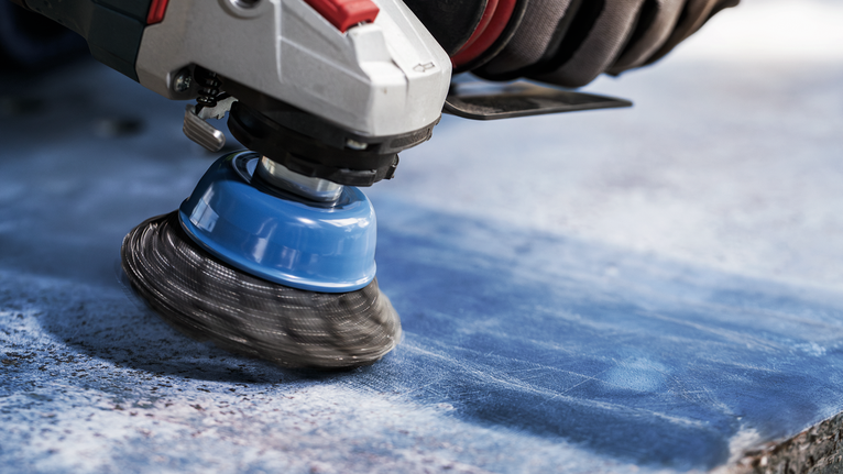 PRO Metal heavy Cup Brush, 75 x 0.5 mm, Thread Person wearing safety equipment uses a rotary brush to clean a stone surface.