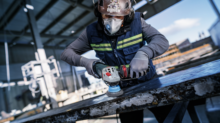 PRO Metal clean Cup Brush, 70 x 0.30 mm, Thread A person wearing safety equipment grinds a large metal sheet at a construction site.