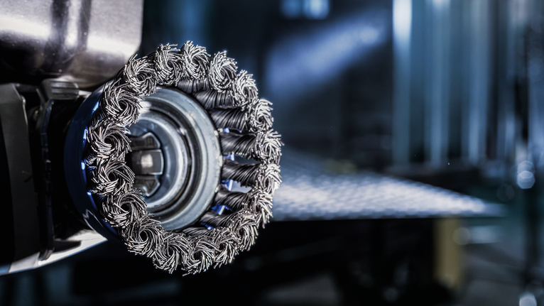 PRO Stainless Steel clean X-Lock Cup Brush, 75 x 0.3 mm Close-up of a wire brush wheel attachment on a power tool in a workshop.